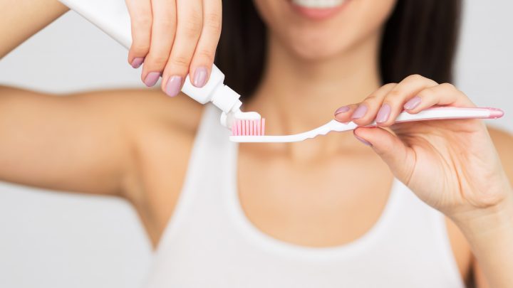 femme souriant appliquant dentifrice sur sa brosse à dents