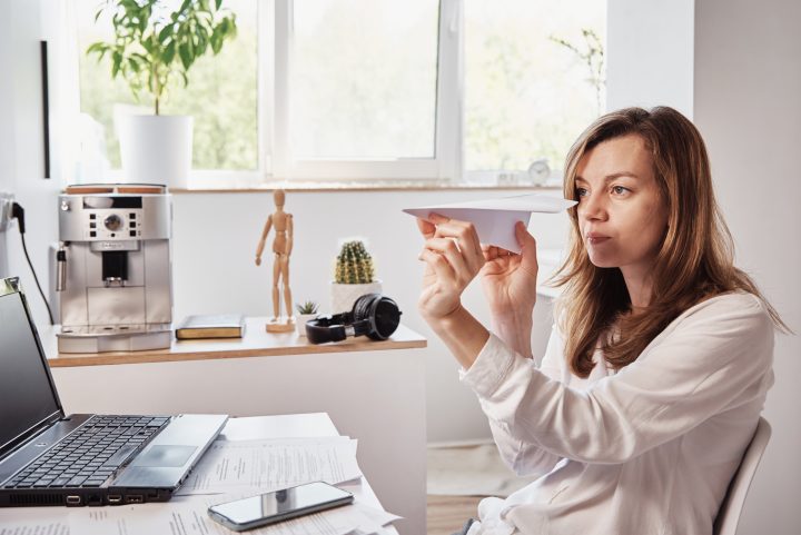 femme procrastinant avec un avion en papier au lieu de travailler